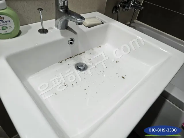 배수구 주변에 이물이 흩어진 사각 세면대